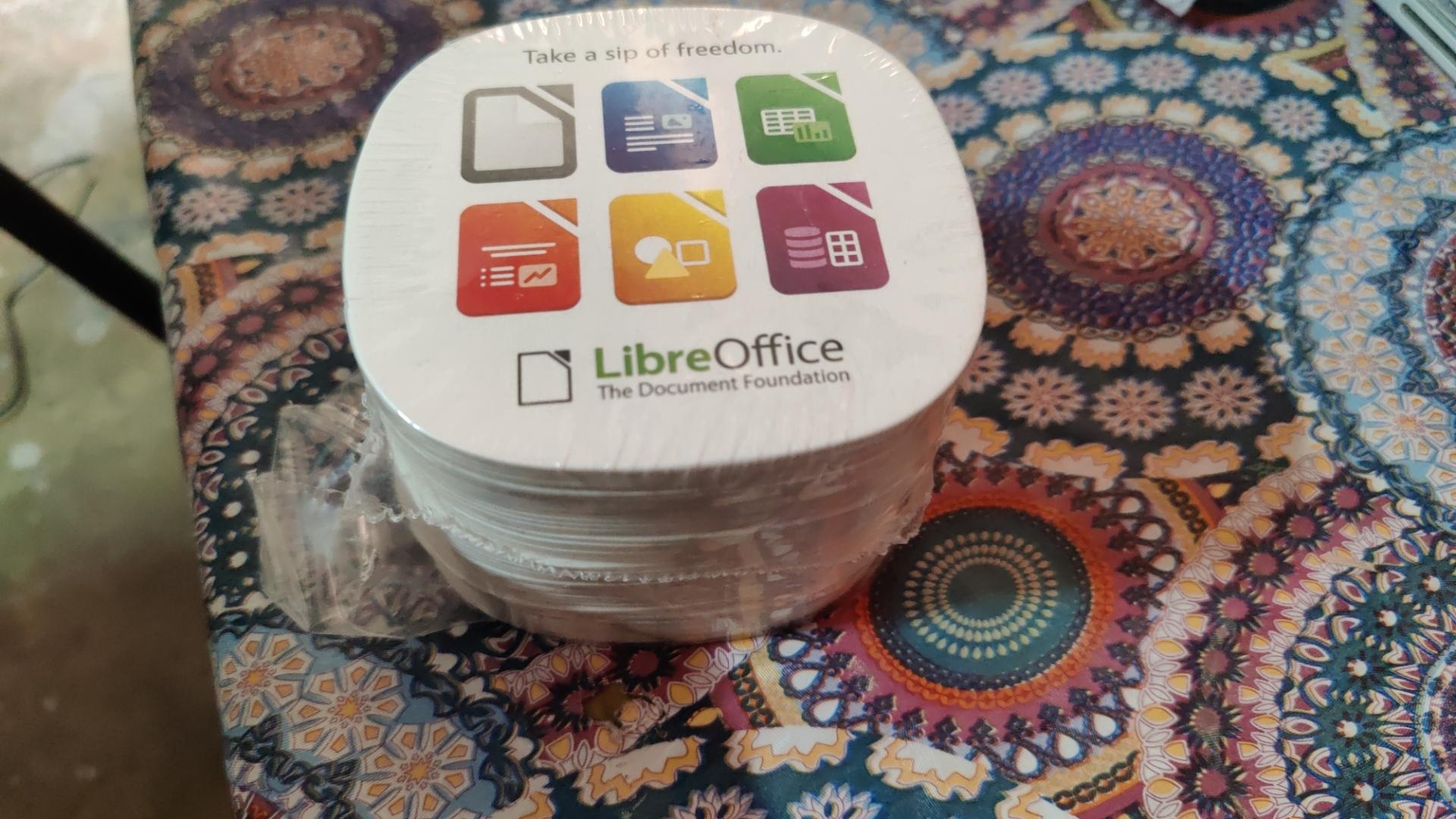 A pack of coasters. Each coaster have  "Take a sip of freedom" written on it, followed by 6 logos of LibreOffice software. At the bottom is the LibreOffice logo, alongside text "LibreOffice" and "The Document Freedom".